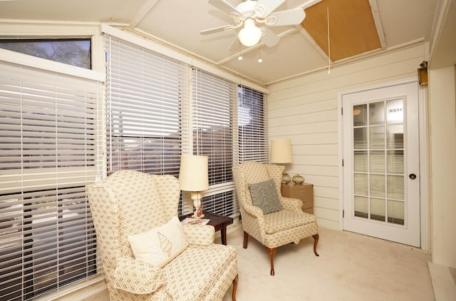 living area with vaulted ceiling, light carpet, ornamental molding, wooden walls, and ceiling fan