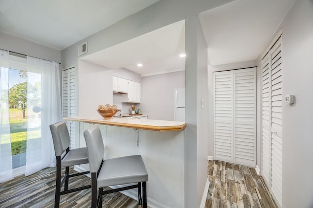 kitchen featuring kitchen peninsula, a breakfast bar, white fridge, white cabinets, and dark hardwood / wood-style floors