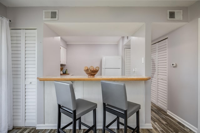 kitchen with white cabinetry, dark hardwood / wood-style floors, white fridge, kitchen peninsula, and a breakfast bar area