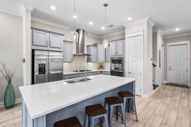 kitchen with a breakfast bar, appliances with stainless steel finishes, a center island with sink, and wall chimney range hood