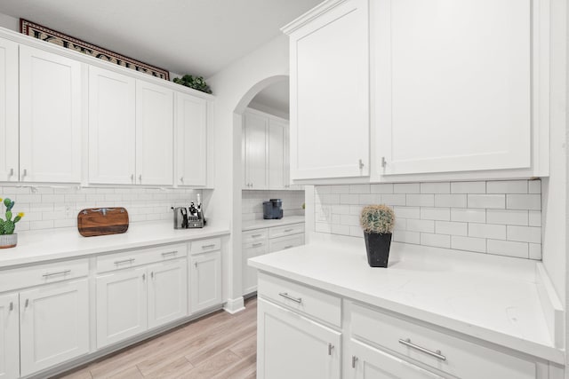 kitchen with backsplash, white cabinetry, light stone counters, and light wood-type flooring