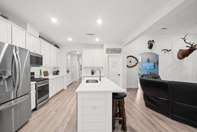 kitchen featuring a center island with sink, white cabinets, appliances with stainless steel finishes, and tasteful backsplash