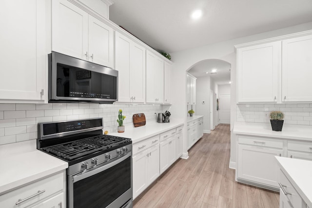 kitchen with tasteful backsplash, white cabinets, stainless steel appliances, and light wood-type flooring