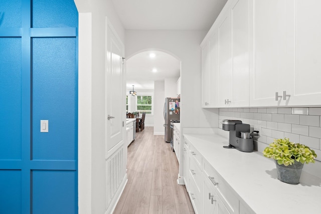 interior space with light wood-type flooring, white cabinetry, stainless steel refrigerator, and backsplash