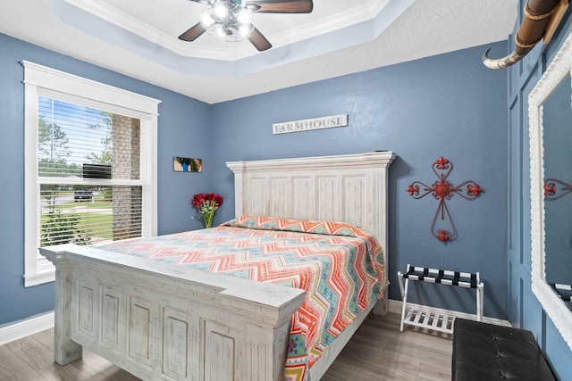 bedroom featuring hardwood / wood-style flooring, ceiling fan, ornamental molding, and a tray ceiling