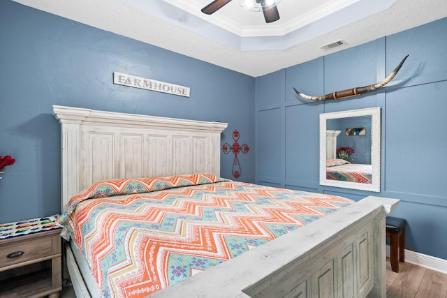 bedroom featuring ceiling fan, light wood-type flooring, ornamental molding, and a tray ceiling