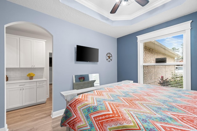 bedroom with ensuite bath, ceiling fan, light wood-type flooring, a tray ceiling, and ornamental molding