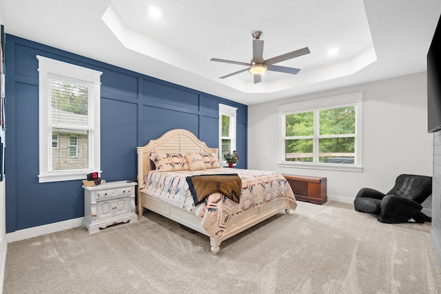 carpeted bedroom featuring a tray ceiling, multiple windows, and ceiling fan