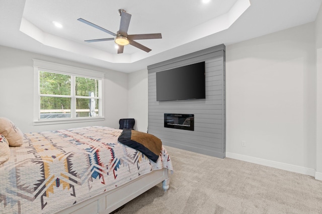 bedroom with ceiling fan, a fireplace, light carpet, and a tray ceiling