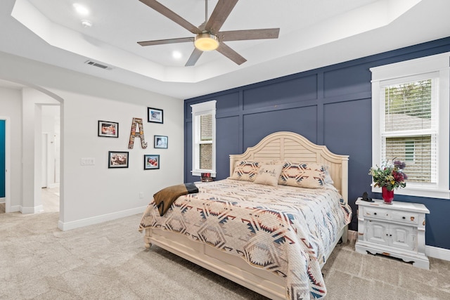 carpeted bedroom featuring a raised ceiling and ceiling fan