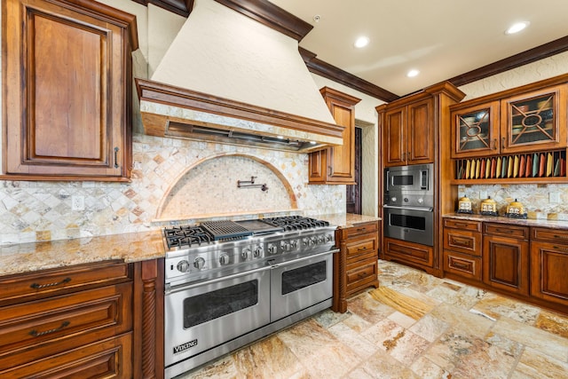 kitchen with light stone countertops, premium range hood, ornamental molding, stainless steel appliances, and brown cabinets