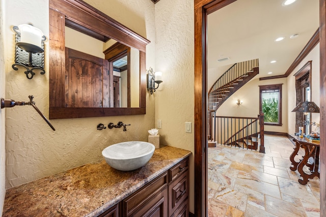 bathroom featuring a sink, stone tile flooring, crown molding, baseboards, and a textured wall