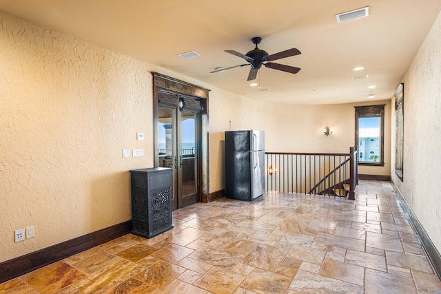 empty room with stone tile floors, baseboards, visible vents, and ceiling fan