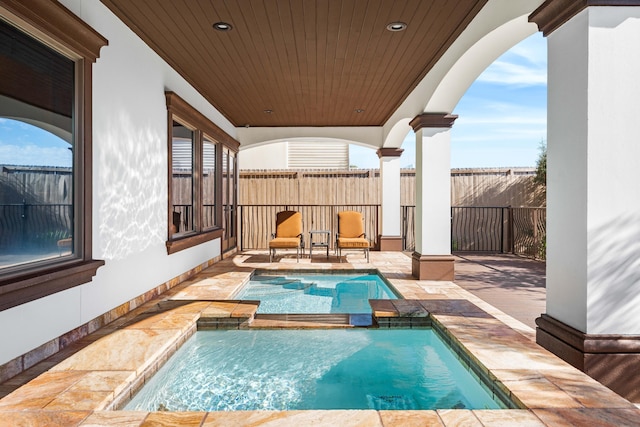 view of pool with a patio area, fence, and a pool with connected hot tub