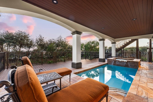 pool at dusk with stairs, a patio, fence, and a pool with connected hot tub