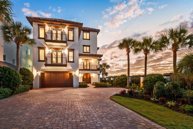 mediterranean / spanish-style home featuring a balcony, driveway, an attached garage, stucco siding, and french doors