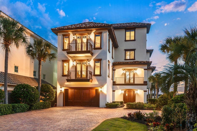 mediterranean / spanish house with a balcony, decorative driveway, french doors, and stucco siding