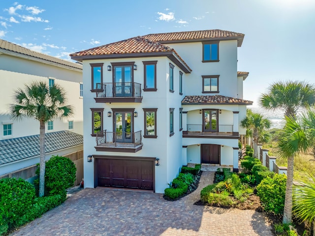 view of front of property with a balcony, stucco siding, french doors, a garage, and decorative driveway