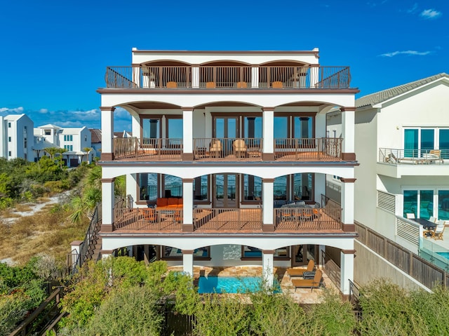 rear view of property with stucco siding, french doors, a balcony, and a patio