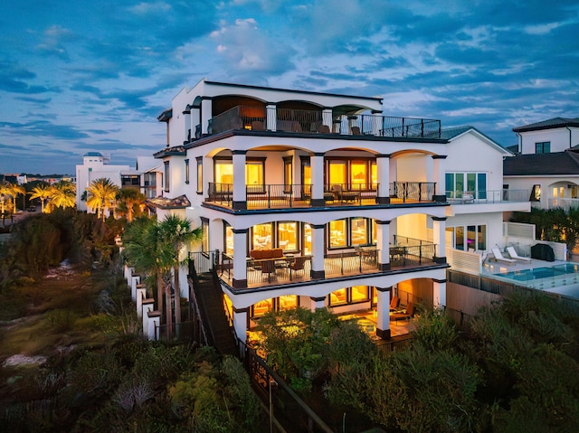 back of house at dusk featuring stucco siding and a balcony