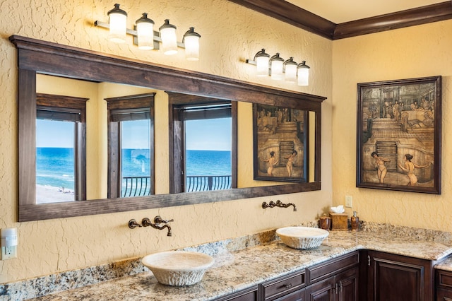 full bathroom featuring double vanity, ornamental molding, a textured wall, and a sink