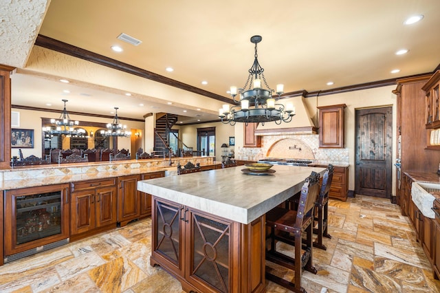 kitchen with stone tile floors, beverage cooler, custom exhaust hood, a large island, and a chandelier