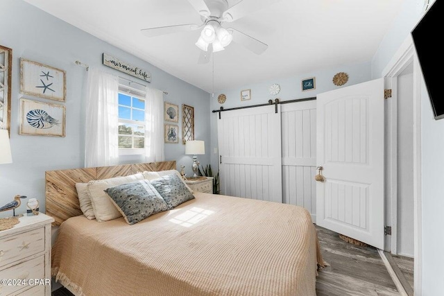 bedroom with a barn door, dark hardwood / wood-style floors, and ceiling fan