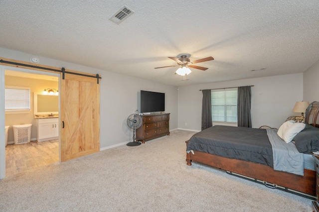 carpeted bedroom with a barn door, ceiling fan, ensuite bath, and a textured ceiling