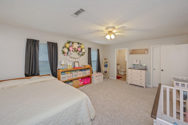 bedroom featuring a textured ceiling, connected bathroom, light colored carpet, and ceiling fan