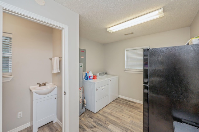 laundry area featuring a textured ceiling, light wood-type flooring, separate washer and dryer, and sink