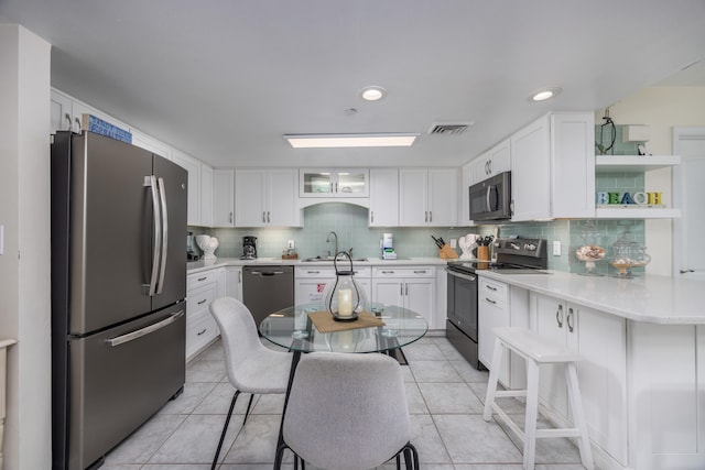 kitchen with white cabinetry, light tile patterned floors, black appliances, and a kitchen breakfast bar