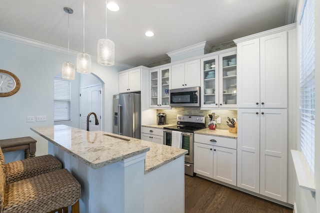 kitchen with white cabinets, a center island with sink, hanging light fixtures, appliances with stainless steel finishes, and light stone countertops