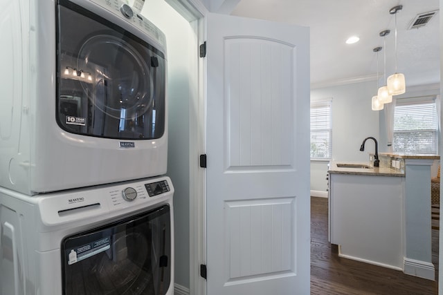 clothes washing area with dark hardwood / wood-style flooring, crown molding, sink, and stacked washer and clothes dryer