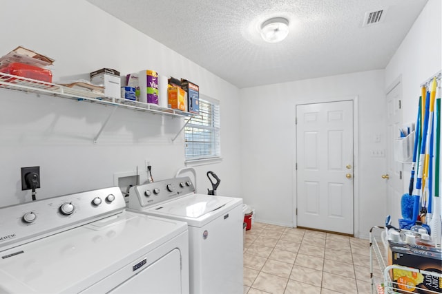 clothes washing area with washer and dryer, light tile patterned floors, and a textured ceiling