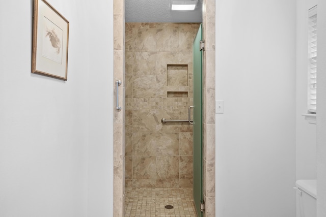 bathroom with a textured ceiling, toilet, and a shower with door