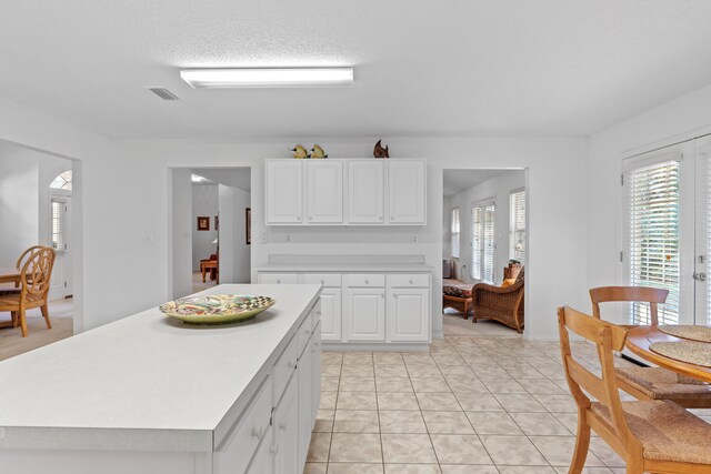 kitchen with a textured ceiling, a center island, white cabinetry, and light tile patterned flooring