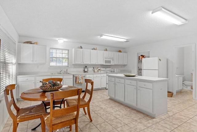 kitchen featuring white appliances, sink, light tile patterned floors, white cabinets, and a center island