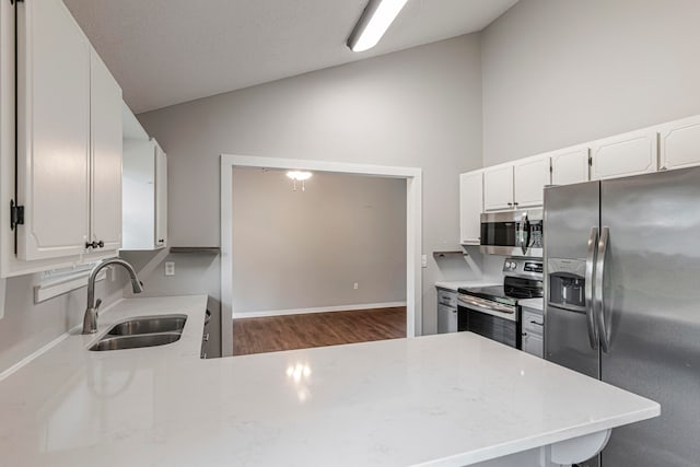 kitchen featuring dark hardwood / wood-style flooring, white cabinets, kitchen peninsula, sink, and appliances with stainless steel finishes