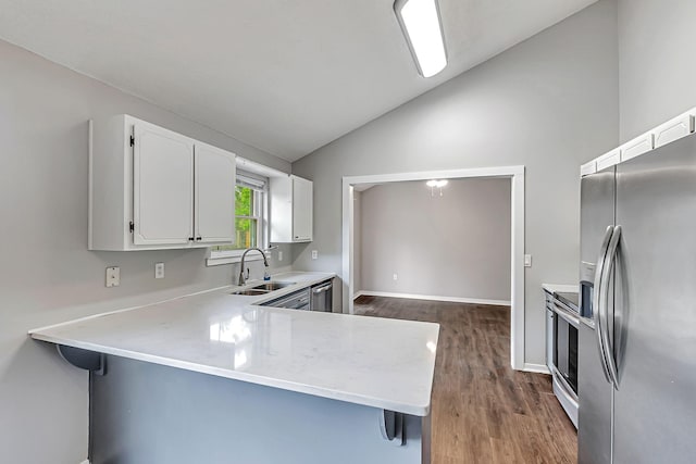 kitchen with appliances with stainless steel finishes, vaulted ceiling, a sink, dark wood-style flooring, and white cabinets