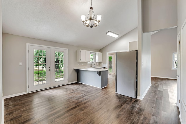 kitchen with freestanding refrigerator, a peninsula, light countertops, a chandelier, and white cabinets