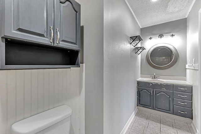 half bath with a textured ceiling, baseboards, toilet, vanity, and ornamental molding