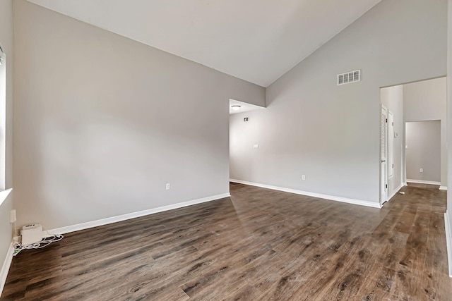 spare room featuring dark wood-style floors, high vaulted ceiling, and baseboards