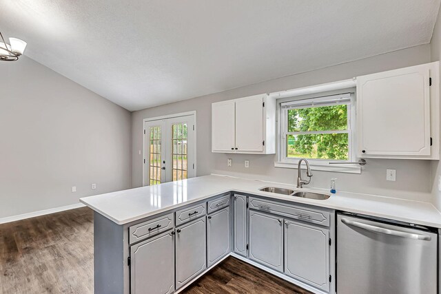 kitchen featuring stainless steel dishwasher, a sink, a peninsula, gray cabinets, and lofted ceiling