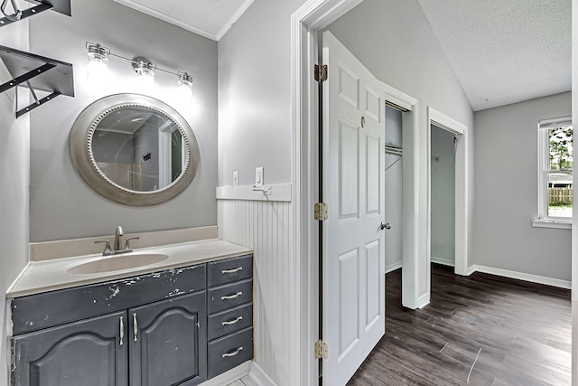 bathroom with a textured ceiling, wood finished floors, baseboards, vaulted ceiling, and vanity