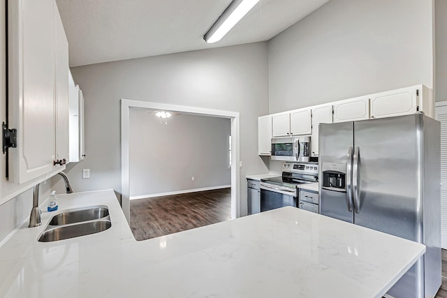 kitchen with appliances with stainless steel finishes, a sink, dark wood finished floors, white cabinets, and vaulted ceiling