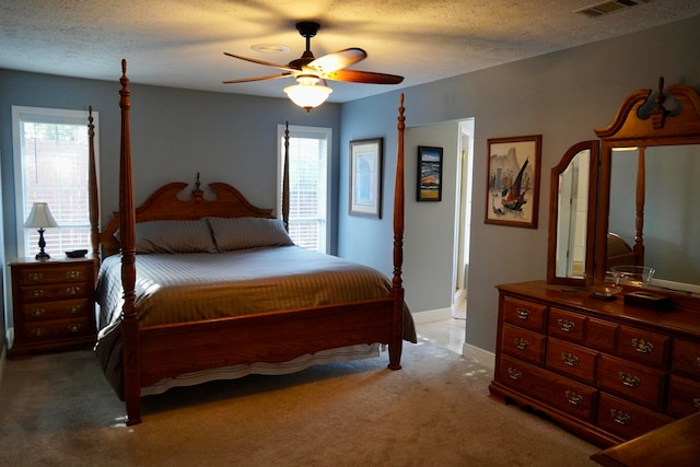 bedroom with a textured ceiling, light colored carpet, and ceiling fan