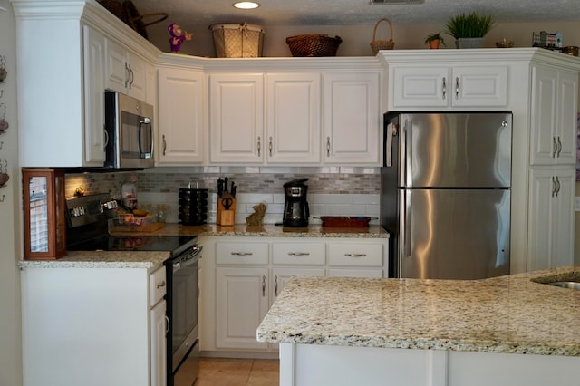 kitchen featuring appliances with stainless steel finishes, light stone countertops, a textured ceiling, light tile patterned floors, and white cabinets