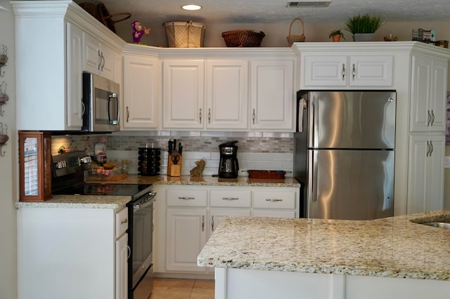 kitchen with white cabinets, stainless steel appliances, light tile patterned floors, and light stone counters