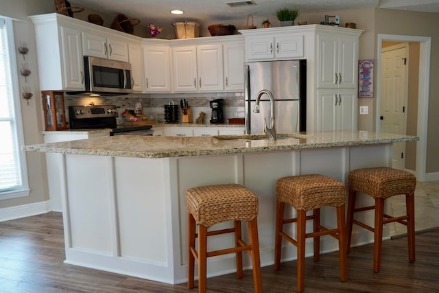 kitchen with white cabinets, appliances with stainless steel finishes, backsplash, and an island with sink