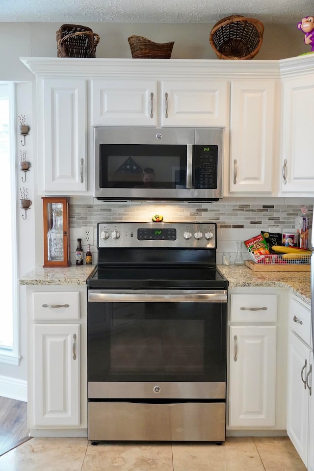 kitchen featuring white cabinets, light stone countertops, backsplash, and appliances with stainless steel finishes